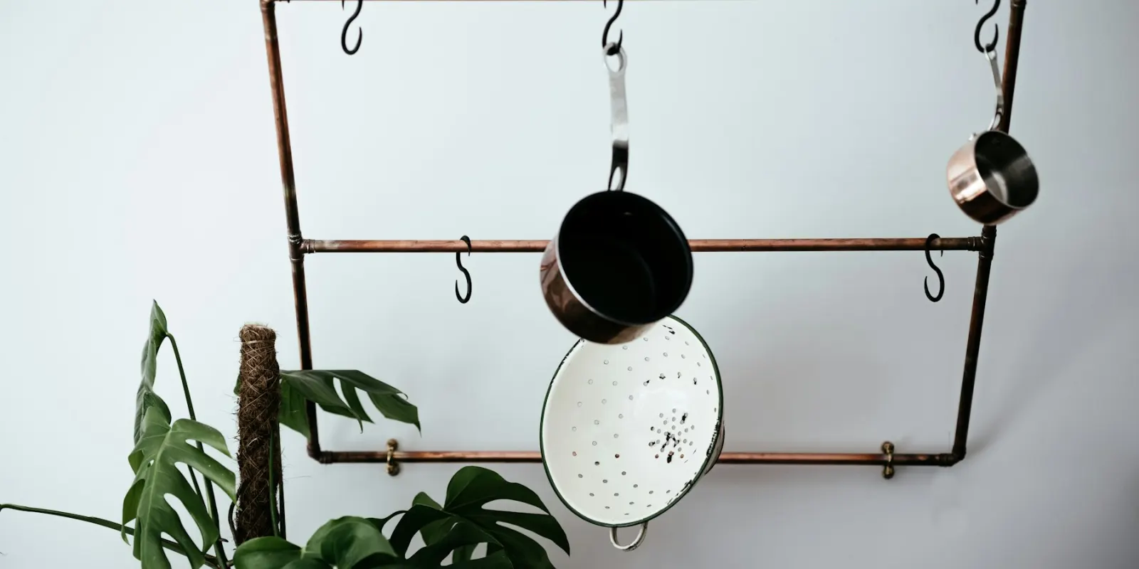 A brass pot rack with a colander and pans